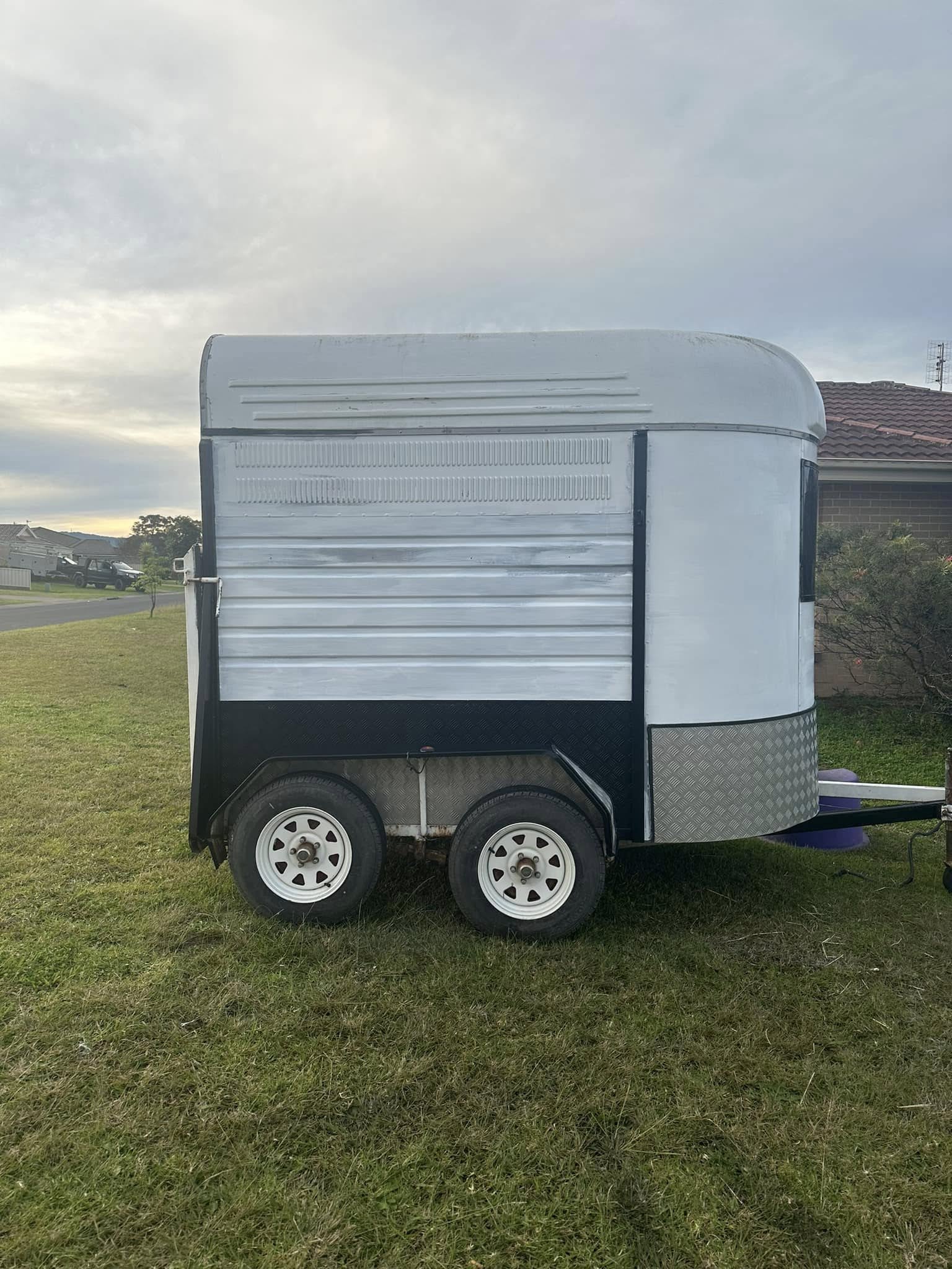 Side of a white tandem-axle horse float with silver panels, parked on grass