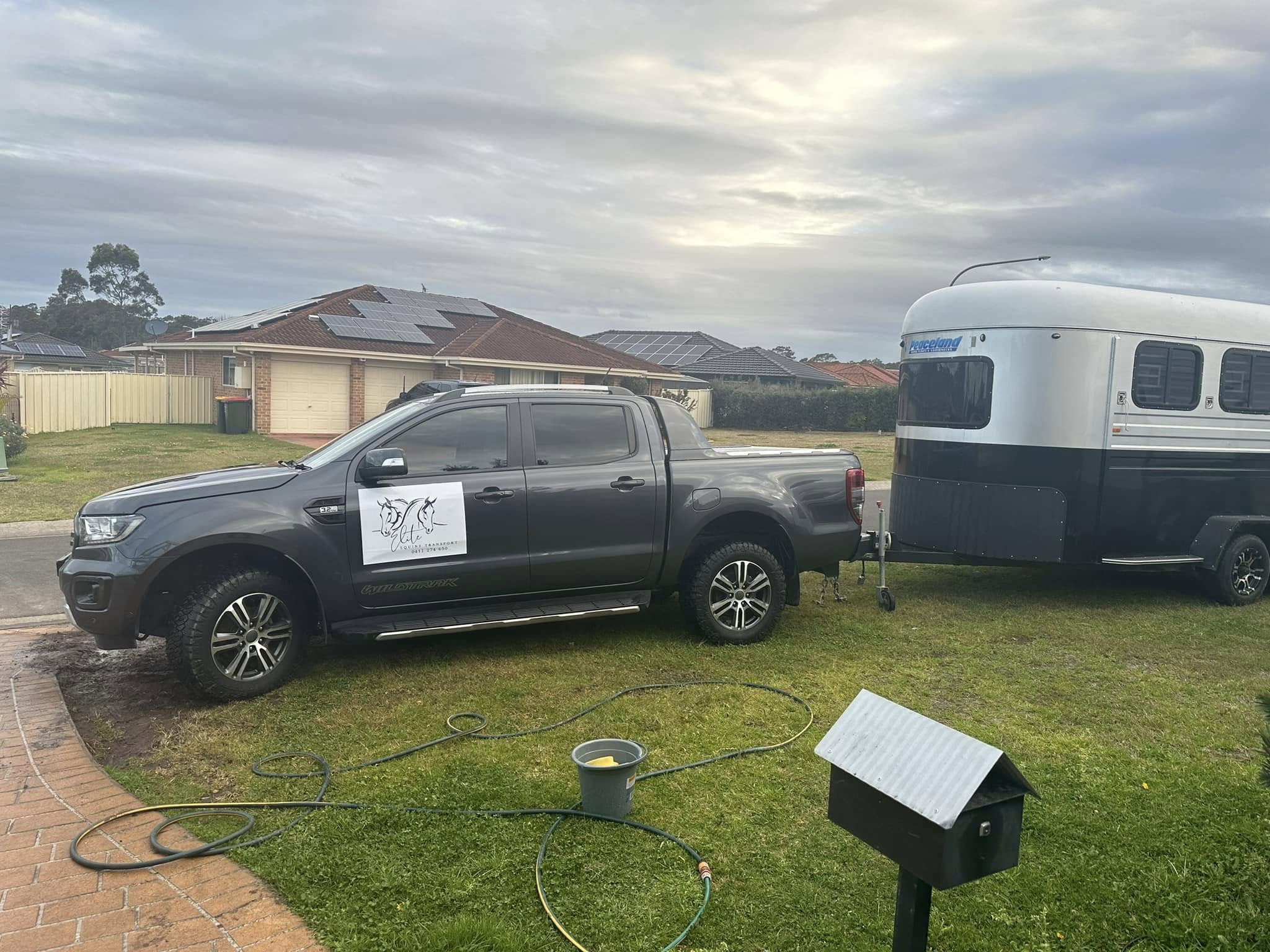 Grey ute on a front lawn with a white and black horse float behind it