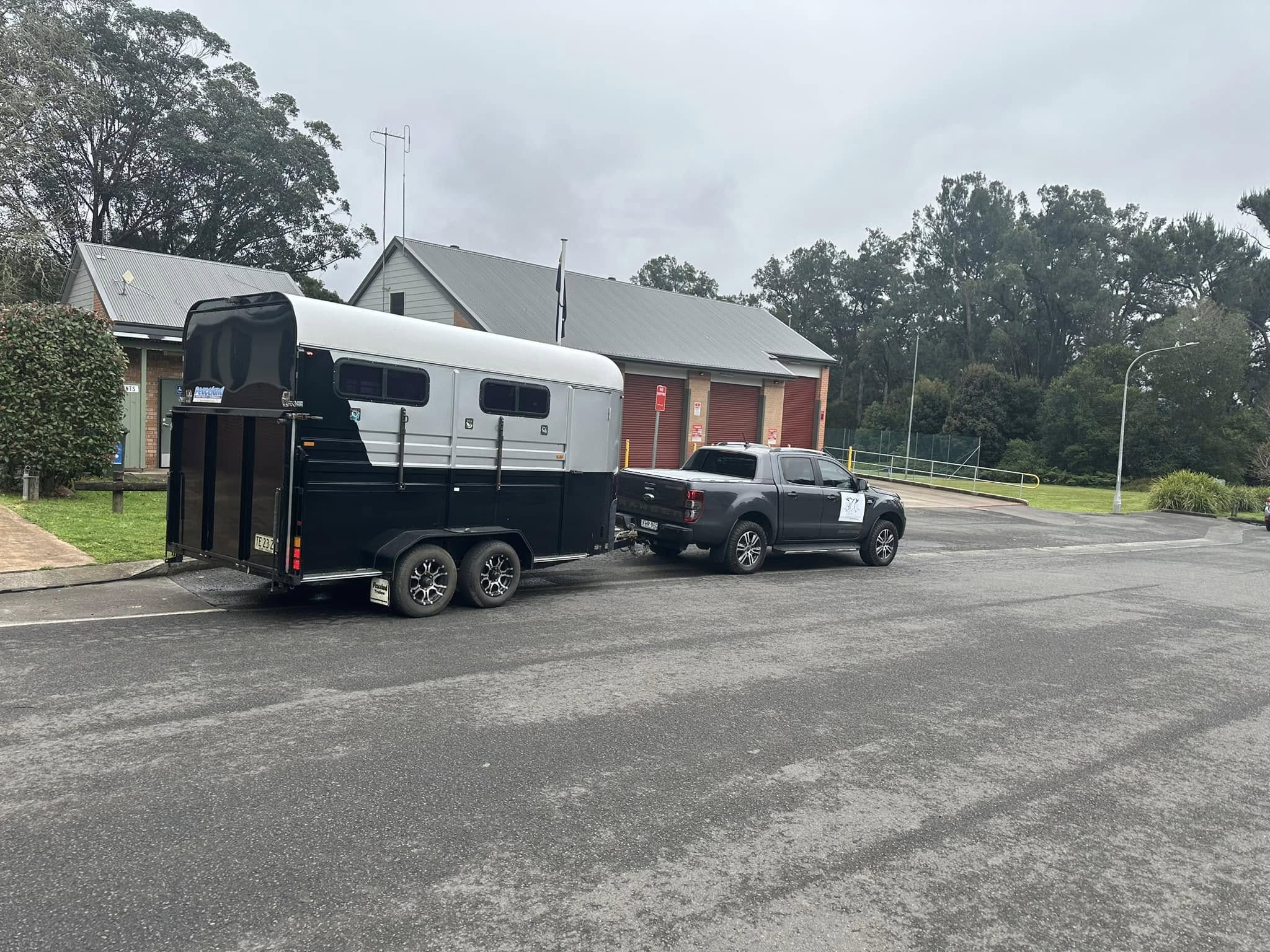 Grey ute towing a black and white horse float, parked on a street